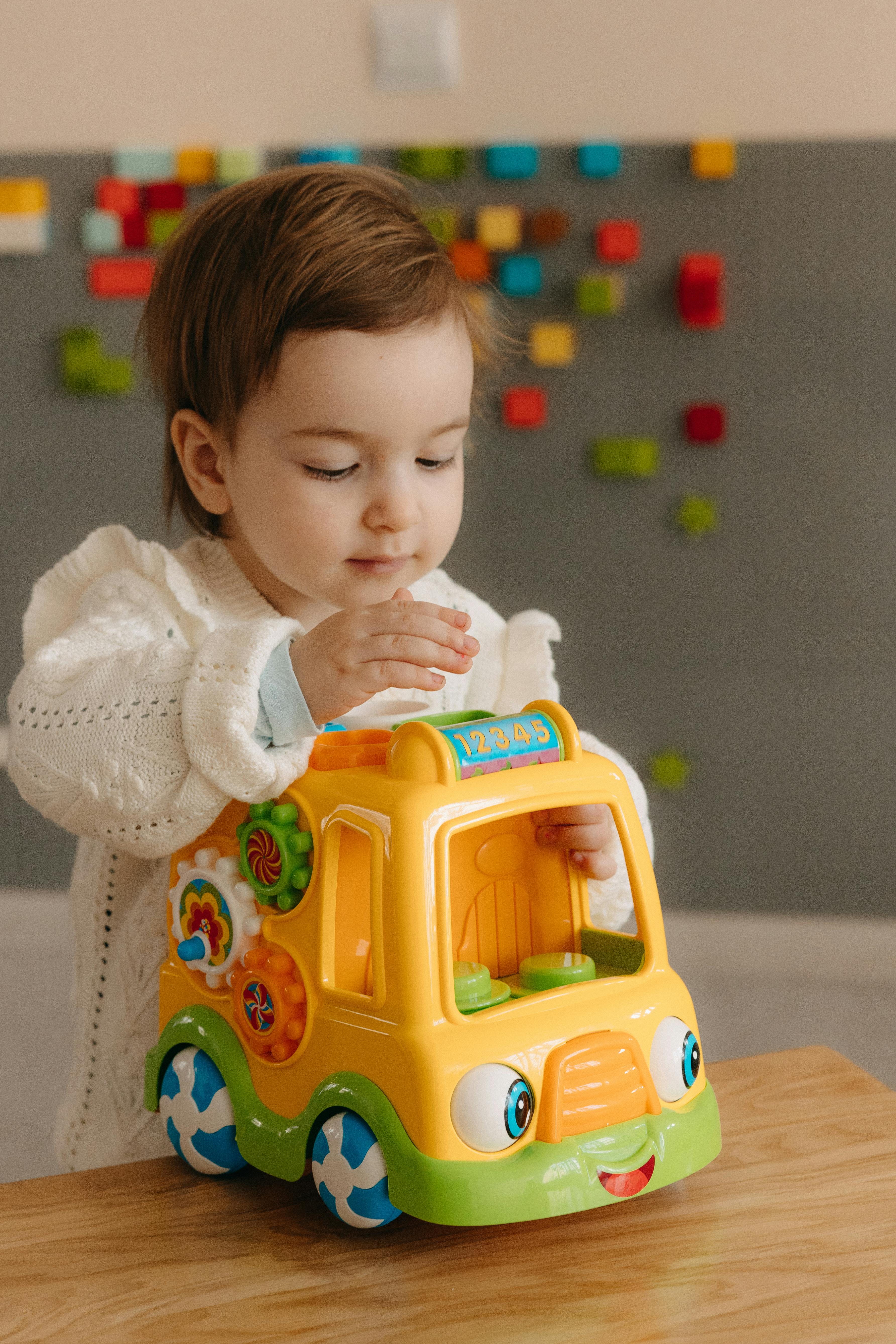 A young child indoors, playing with a cheerful, colorful toy truck, showcasing curiosity and learning.