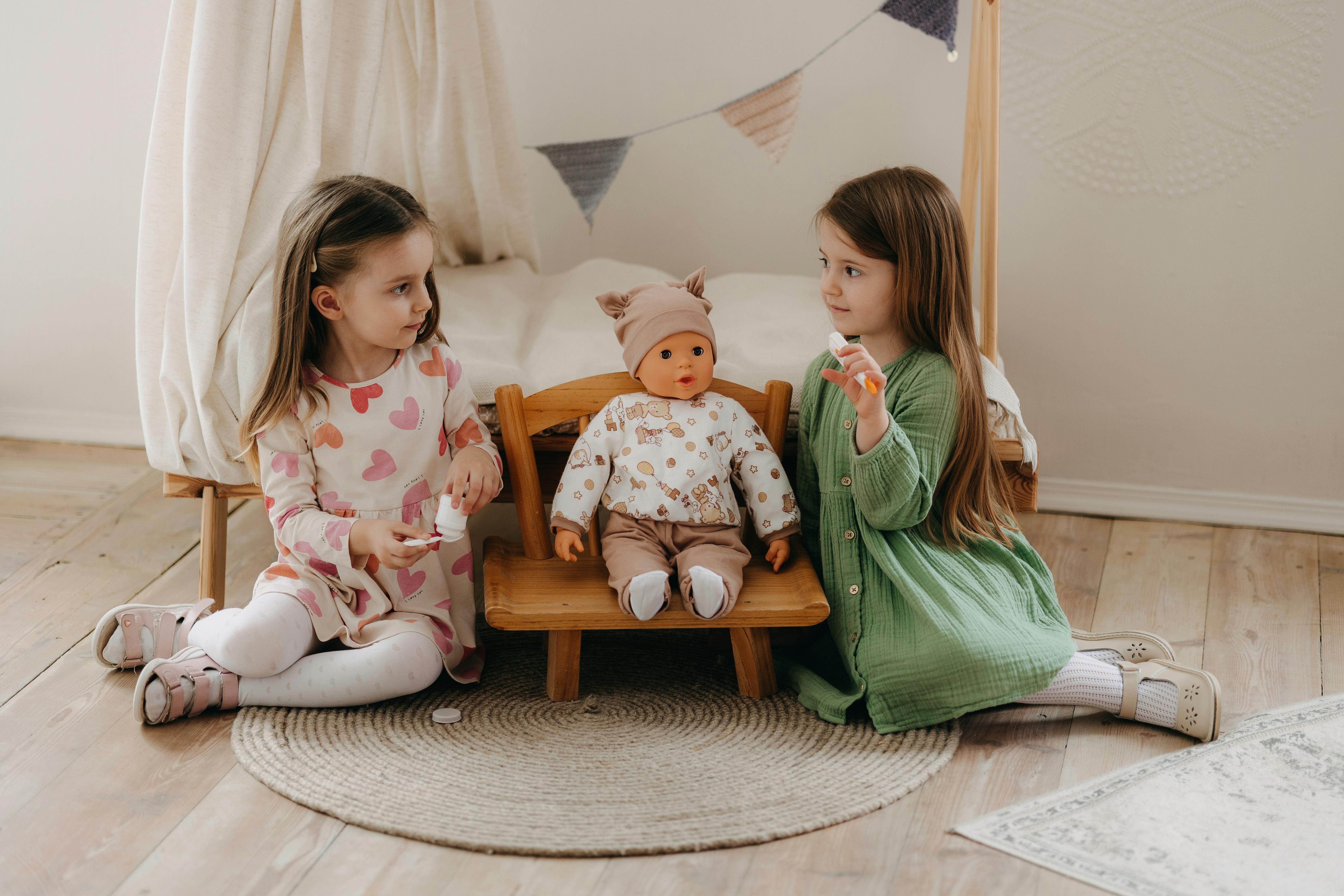 two little girls sitting on a wooden chair with a doll