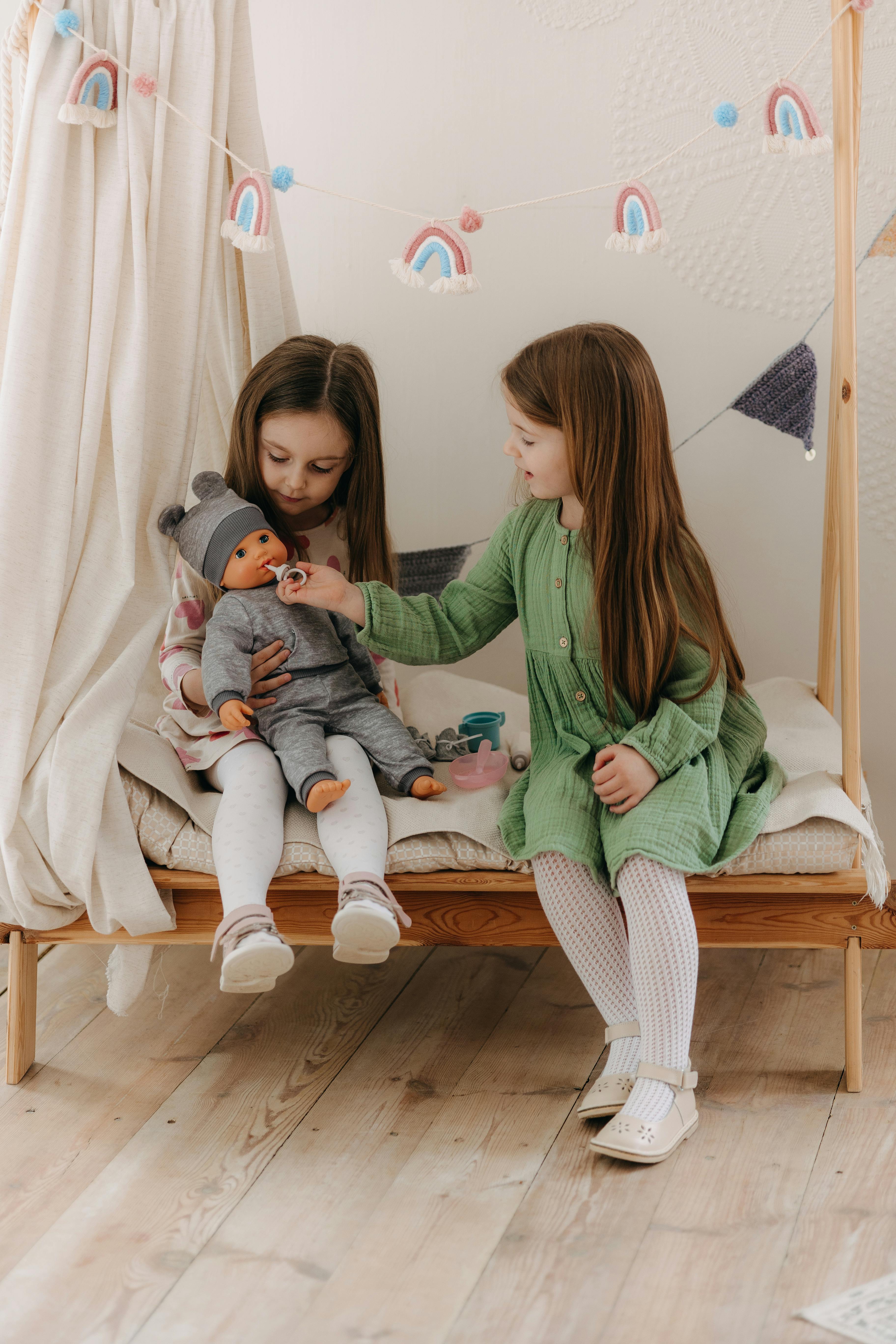 two little girls sitting on a bed with a doll