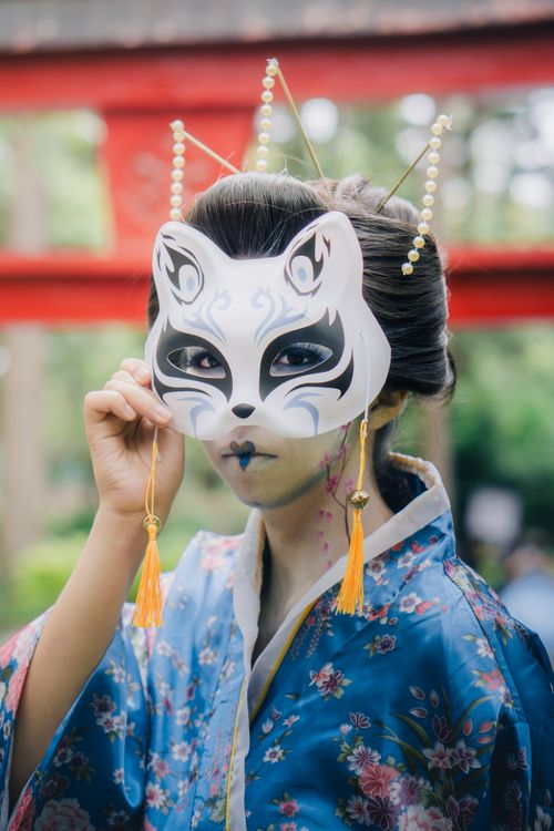 Free Woman wearing a fox mask and traditional attire, set in a vibrant outdoor festival. Stock Photo