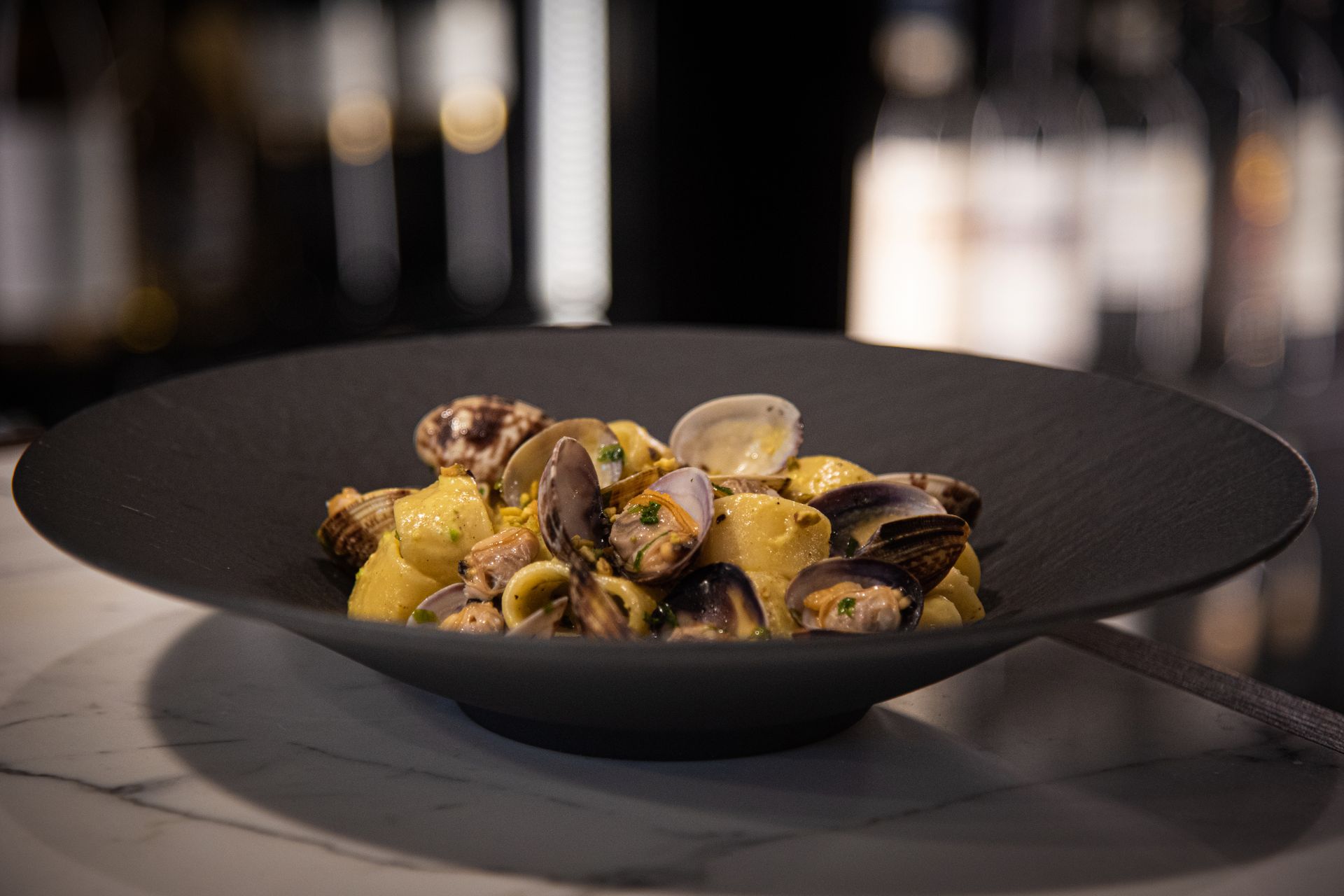 Delicious seafood pasta dish with mussels and clams elegantly presented on a black plate indoors.