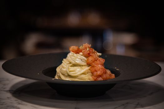 Close-up of spaghetti topped with shrimp and tomato sauce on a black plate.