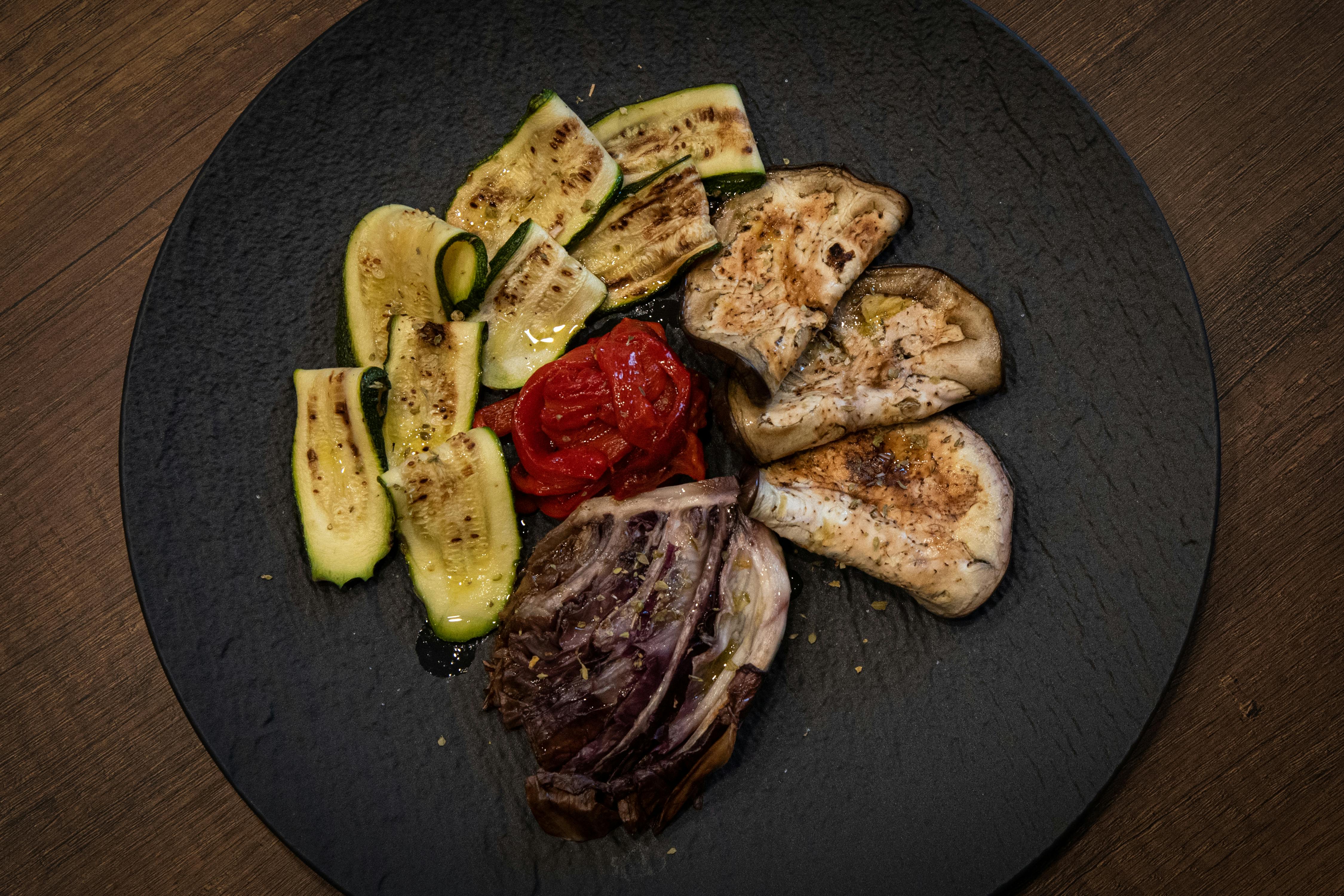 A delectable assortment of grilled vegetables on a rustic black plate, accented with olive oil and spices.