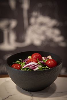 A stylish bowl of fresh vegetable salad featuring tomatoes and greens on a marble surface.
