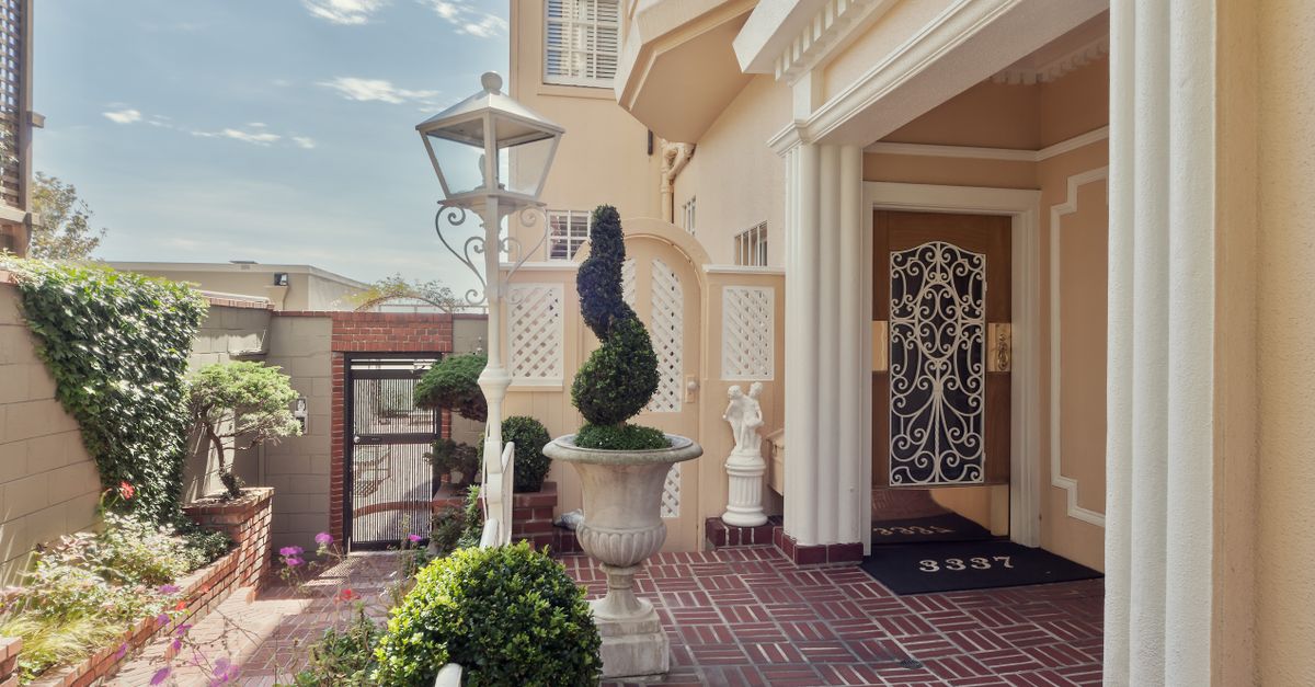 Beautiful luxury home entrance featuring classic columns and topiary in sunny courtyard.