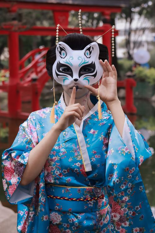 Free Woman in a traditional kimono wearing a fox mask in a Japanese garden setting. Stock Photo