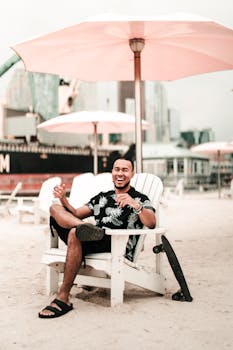 男人在多伦多海滩的遮阳伞下，坐在椅子上微笑放松