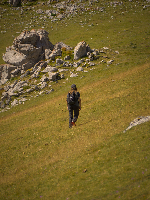 Free Person hiking alone on a grassy rocky hillside under a clear sky. Stock Photo