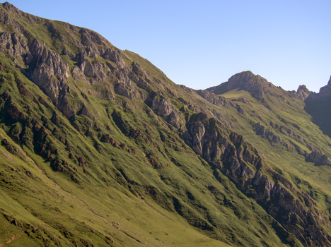 A serene mountain landscape with lush green slopes and craggy peaks under a clear sky.