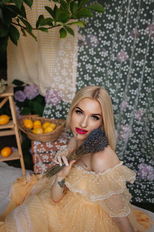 Free Blonde woman in a yellow dress holding flowers, surrounded by floral decor and lemons. Stock Photo