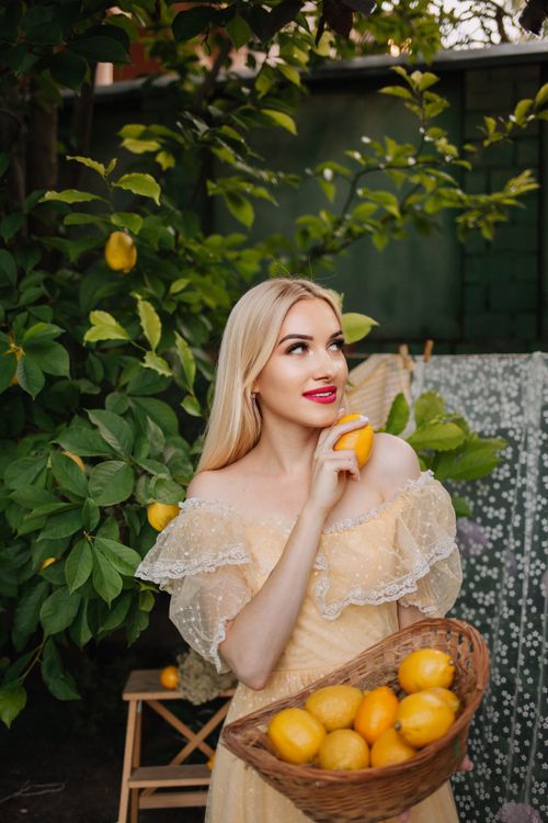 Free Woman in yellow dress holding lemons in a lush summer garden. Stock Photo