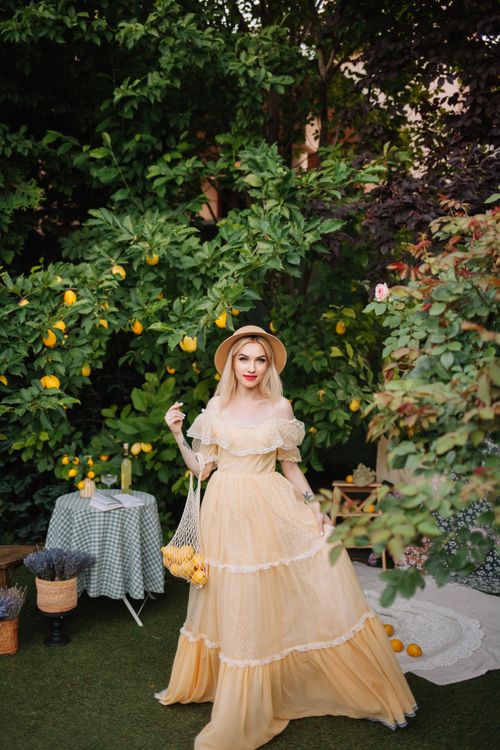 Free Woman in a flowing dress poses gracefully amidst a lush lemon garden. Stock Photo