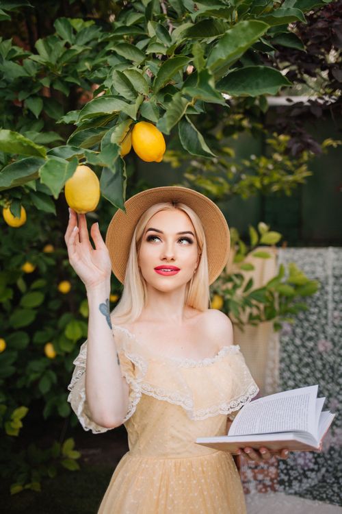 Free Elegant woman in a summer dress picking lemons, book in hand. Perfect for lifestyle and fashion themes. Stock Photo