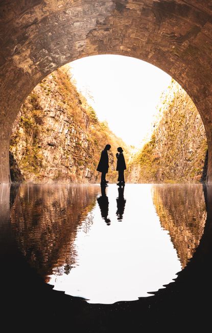 Romantic silhouette of a couple in tunnel with water reflection.