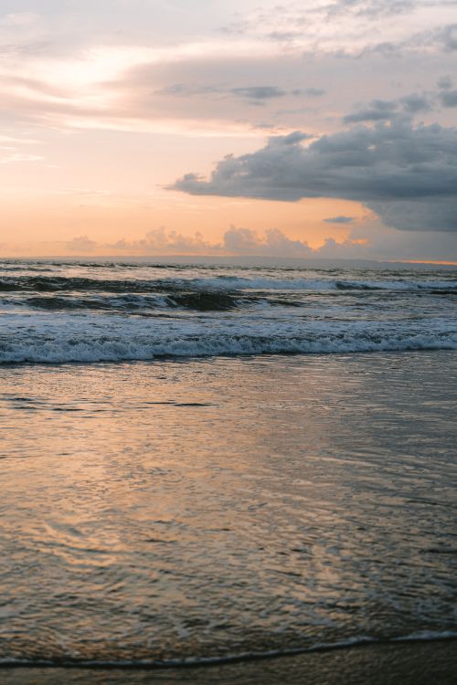Free A tranquil Bali beach captured at sunset, showcasing the gentle waves and pastel sky reflections. Stock Photo