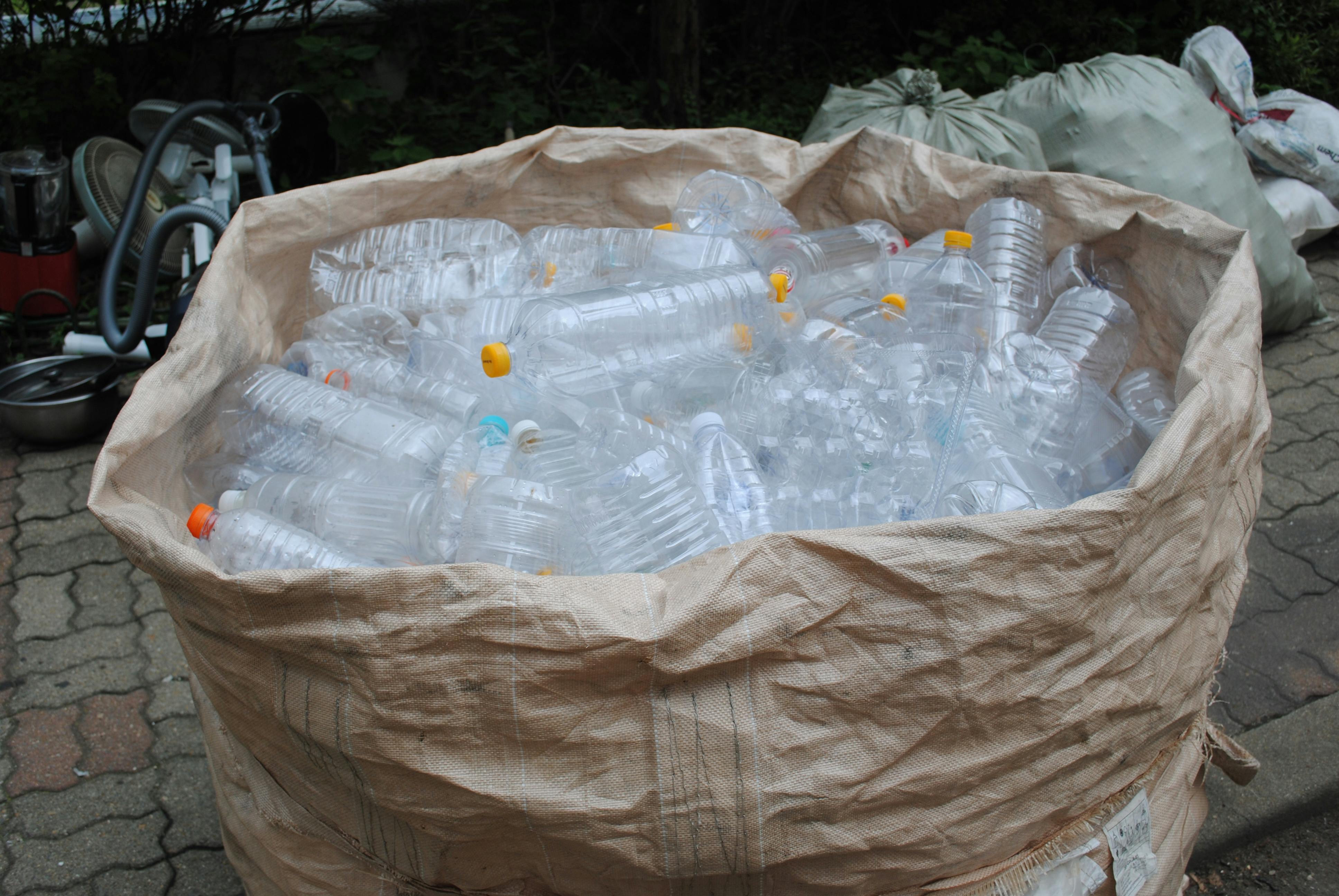 A filled bag of plastic bottles ready for recycling in an outdoor setting.