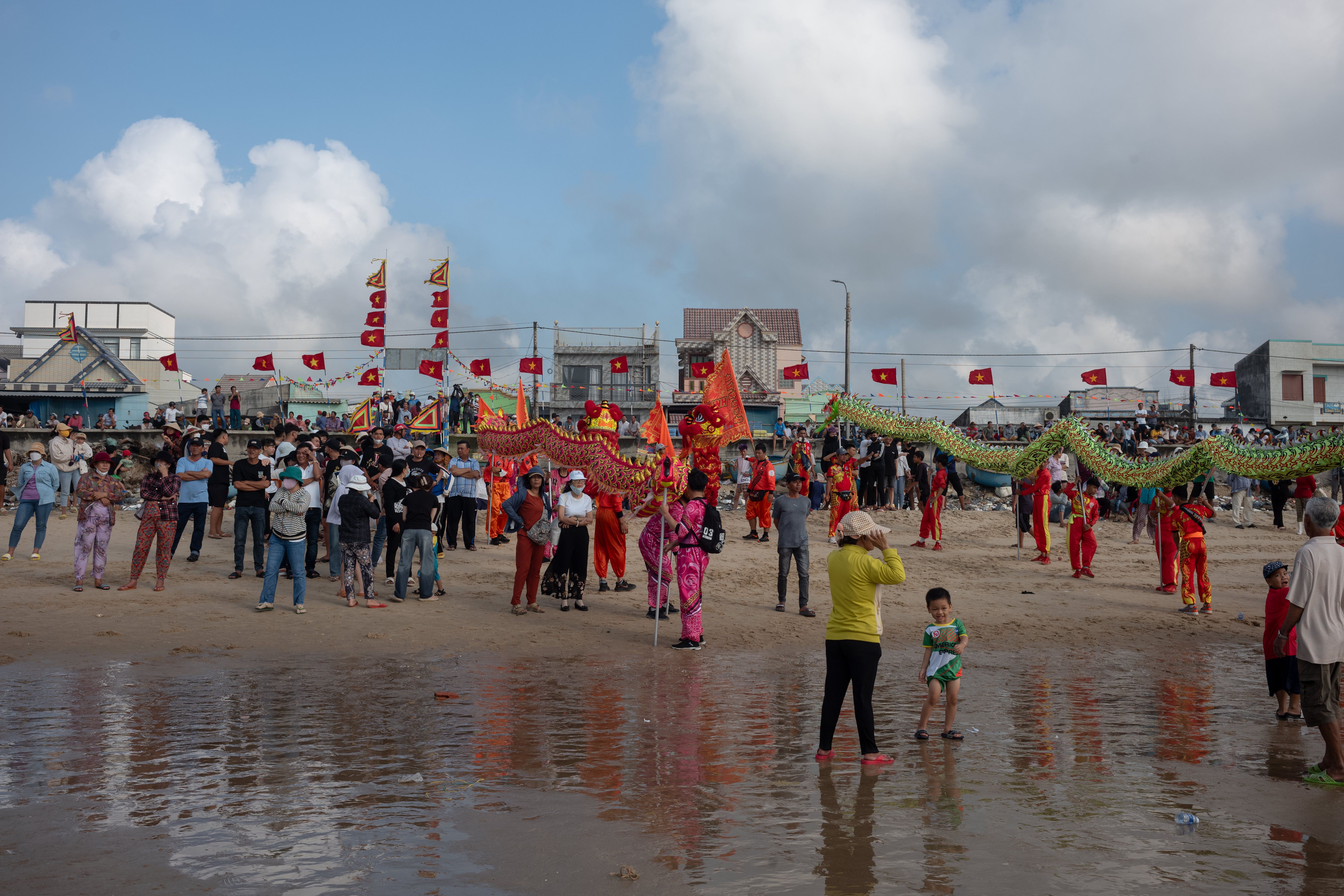 Colorful lion dance celebration with crowds and Vietnamese flags on Vũng Tàu beach.