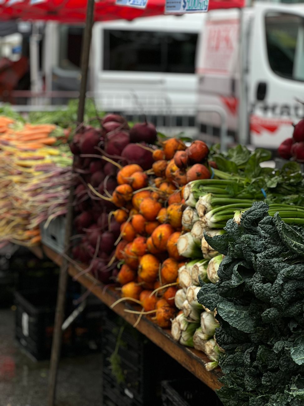 A vibrant display of fresh root vegetables and greens at an outdoor farmer's market, perfect for healthy living content.. pex
