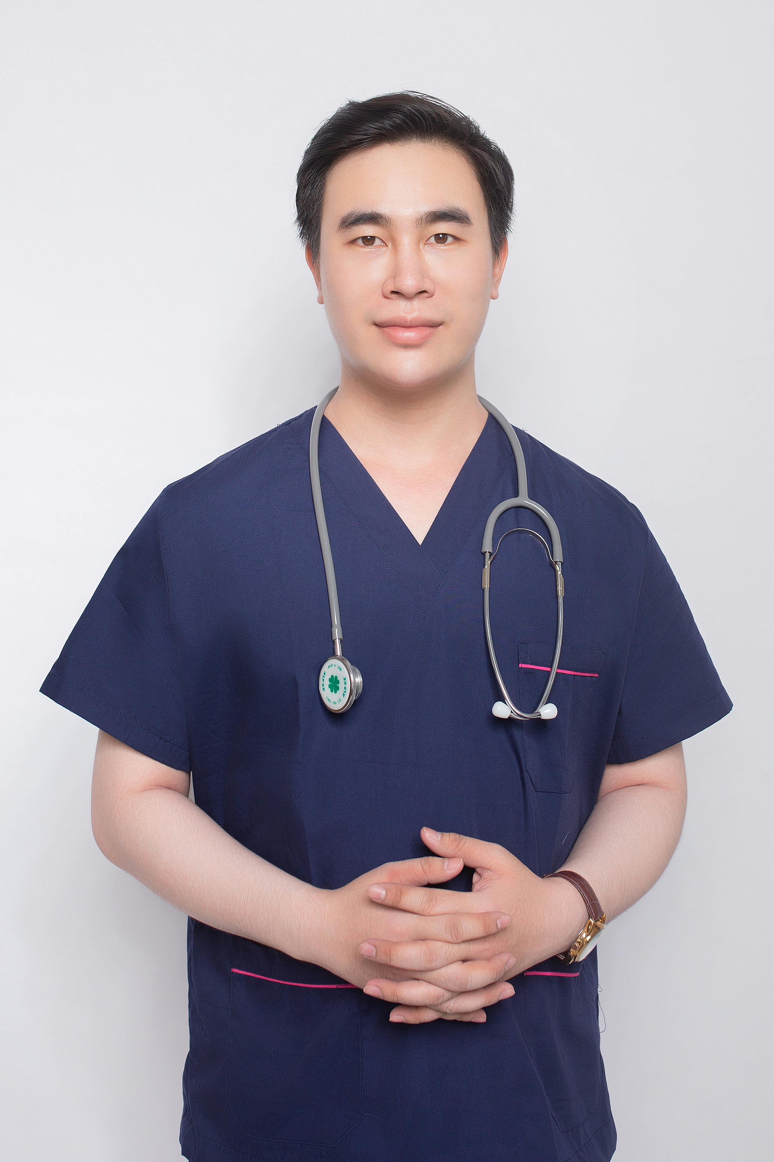 A smiling male doctor in scrubs, confidently posing with a stethoscope indoors.