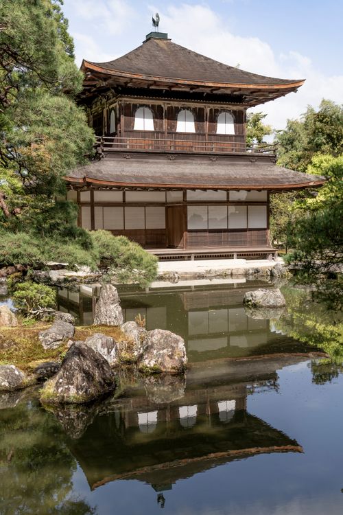Free A serene Japanese temple reflected in a pond surrounded by lush greenery, showcasing traditional architecture. Stock Photo