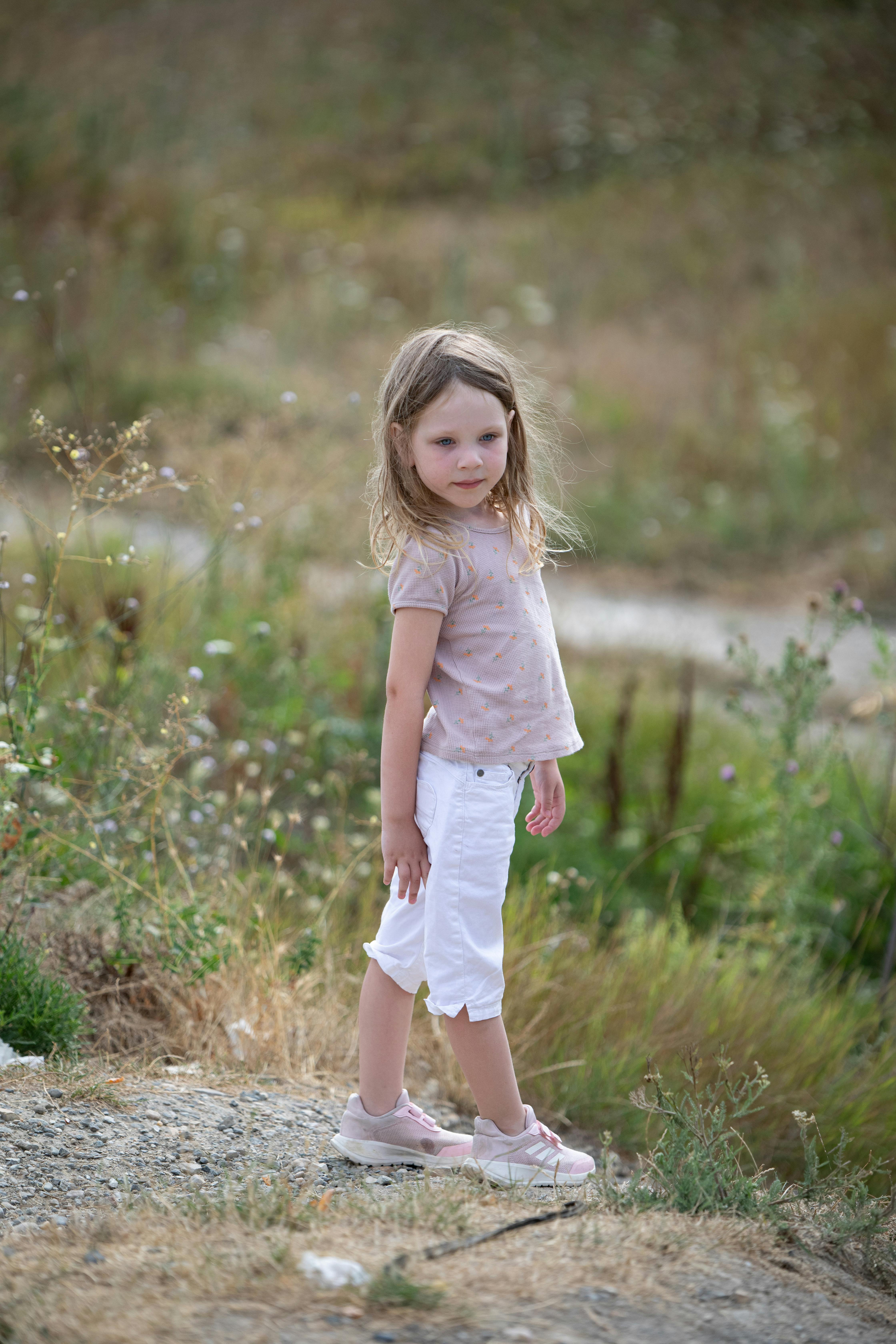 a little girl standing on a hill with grass and flowers