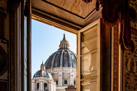 A stunning view of St. Peter's Basilica dome through an ornate window in Vatican City.