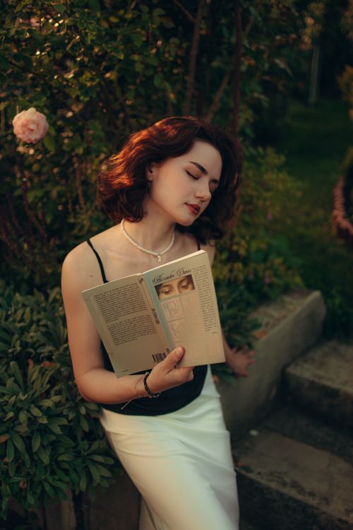 Free A woman enjoys a tranquil moment reading outdoors in a lush summer garden. Stock Photo