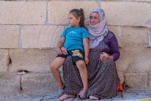 A woman and child sitting on the ground next to a wall