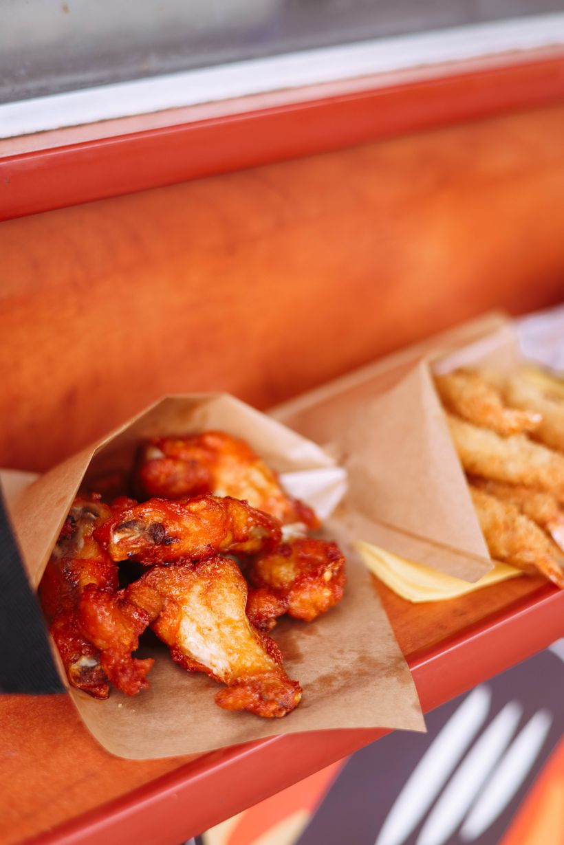 Halal chicken wings tossed in sauce served in a kraft paper boat with a side of fries