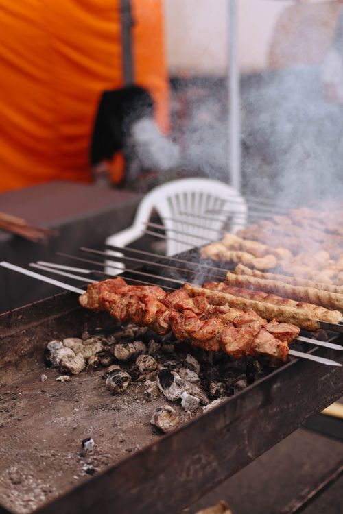 Free Skewered meat grilling over hot coals with smoke rising, perfect for a BBQ picnic. Stock Photo