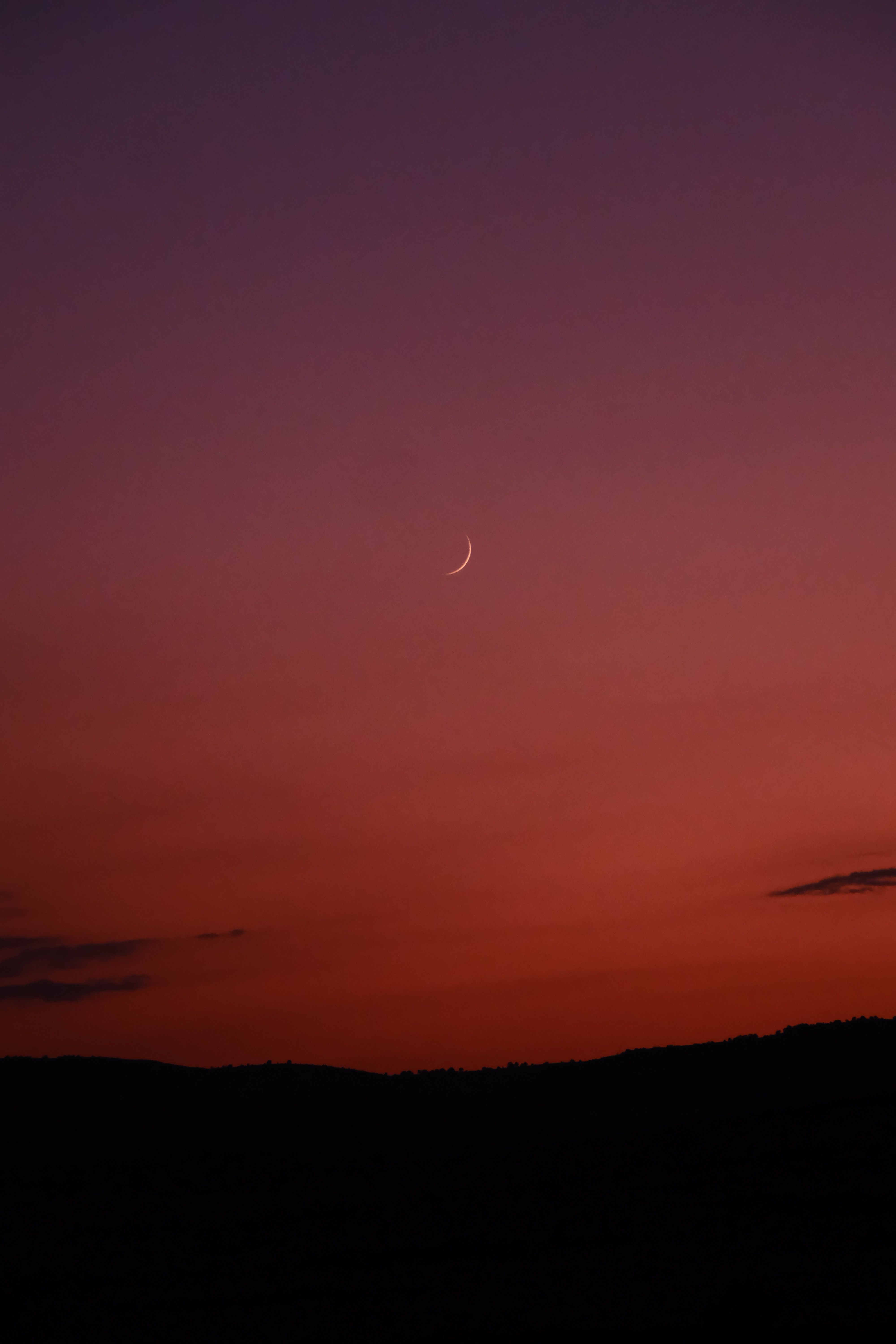 A tranquil view of a crescent moon against a gradient evening sky during twilight.