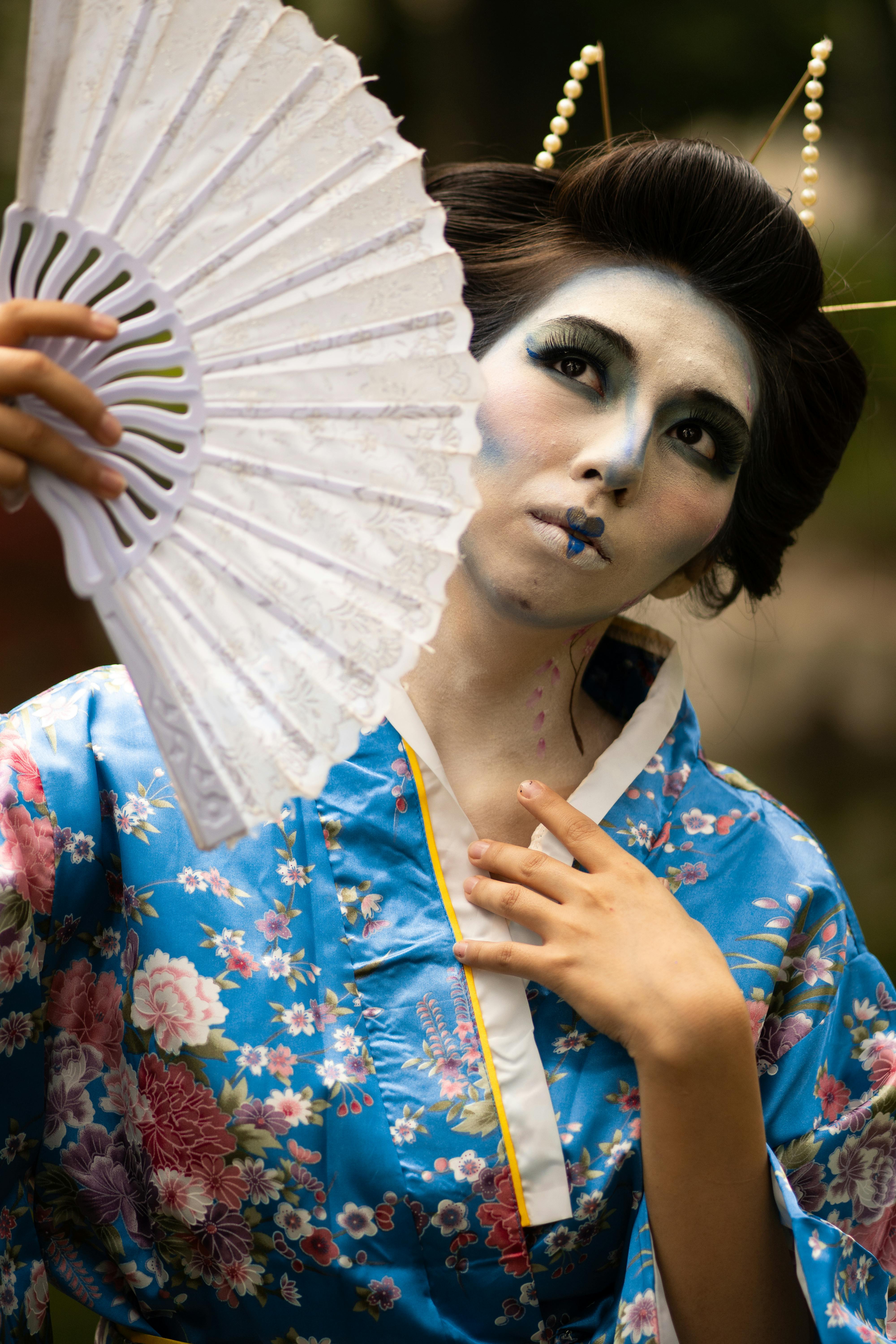 A colorful portrait of a woman in traditional geisha attire with creative makeup in a public park.