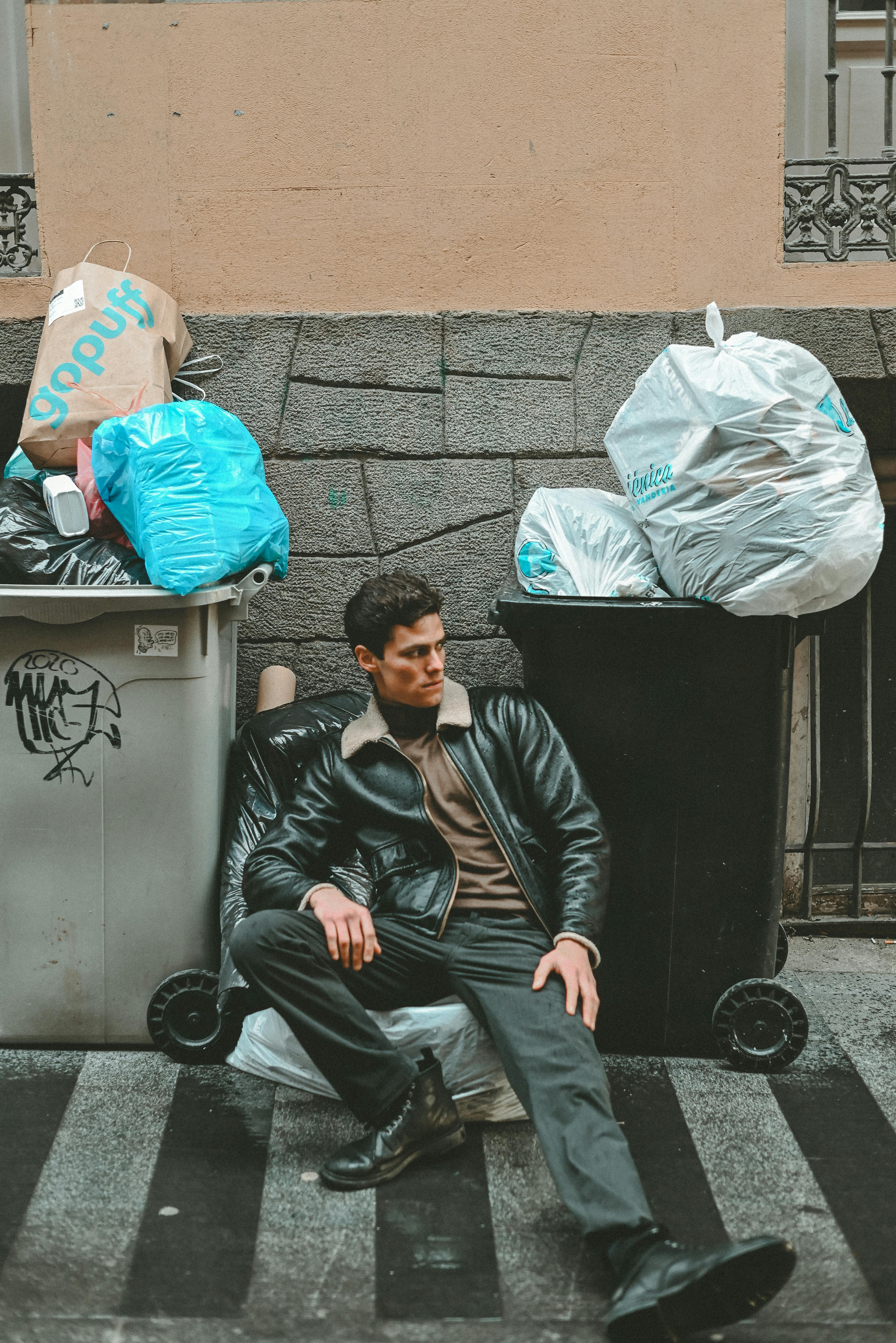 A man sitting on the curb next to a trash can