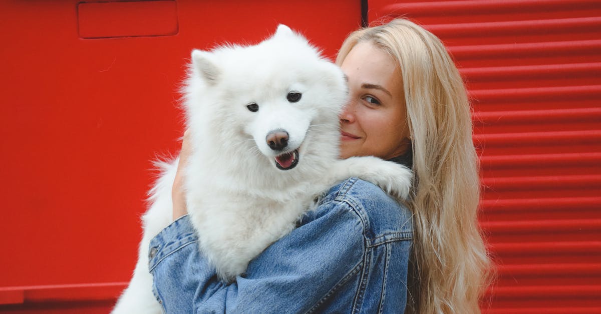 A woman holding a white dog in front of a red wall