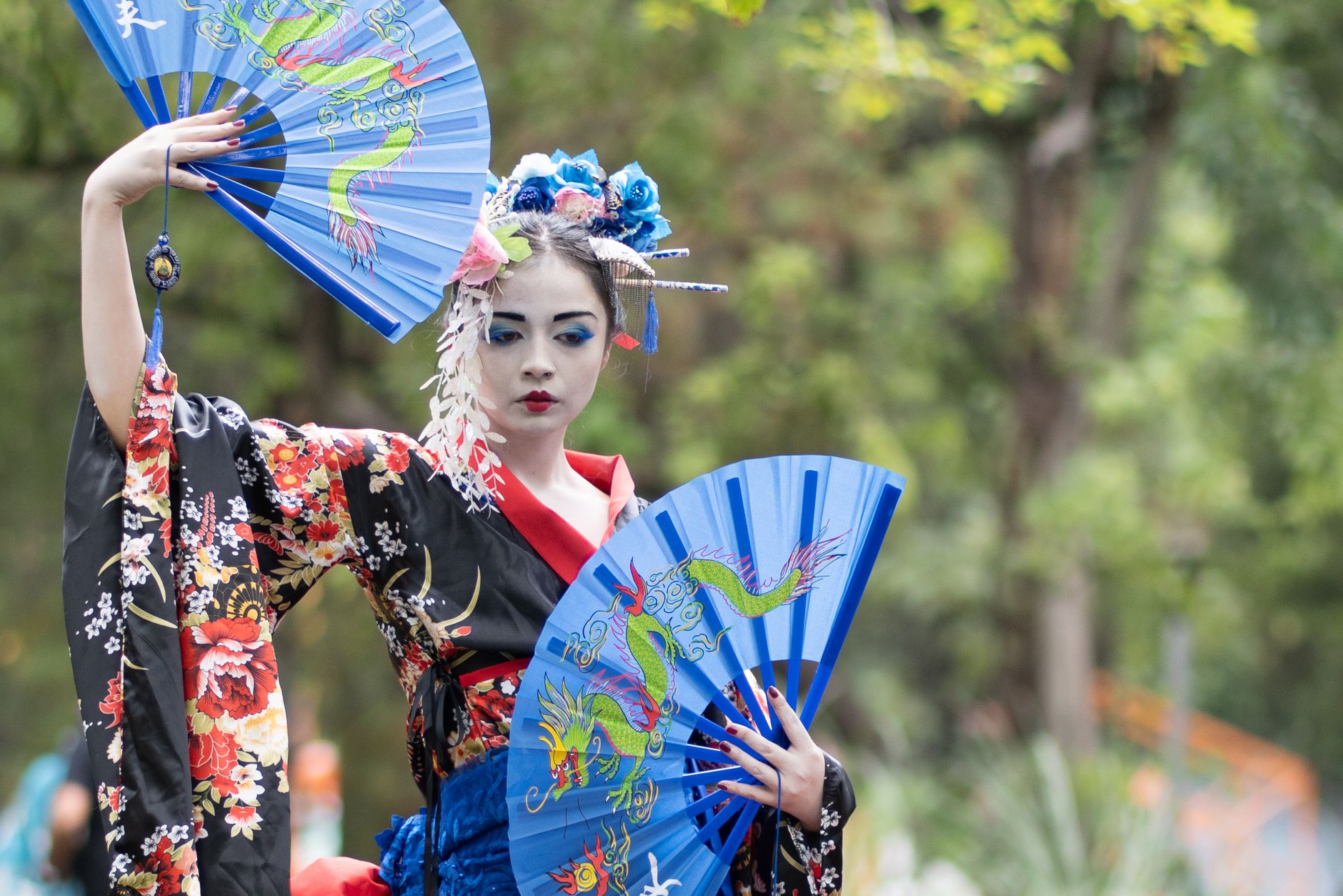 Vibrant geisha-inspired portrait with artistic makeup in a public park.