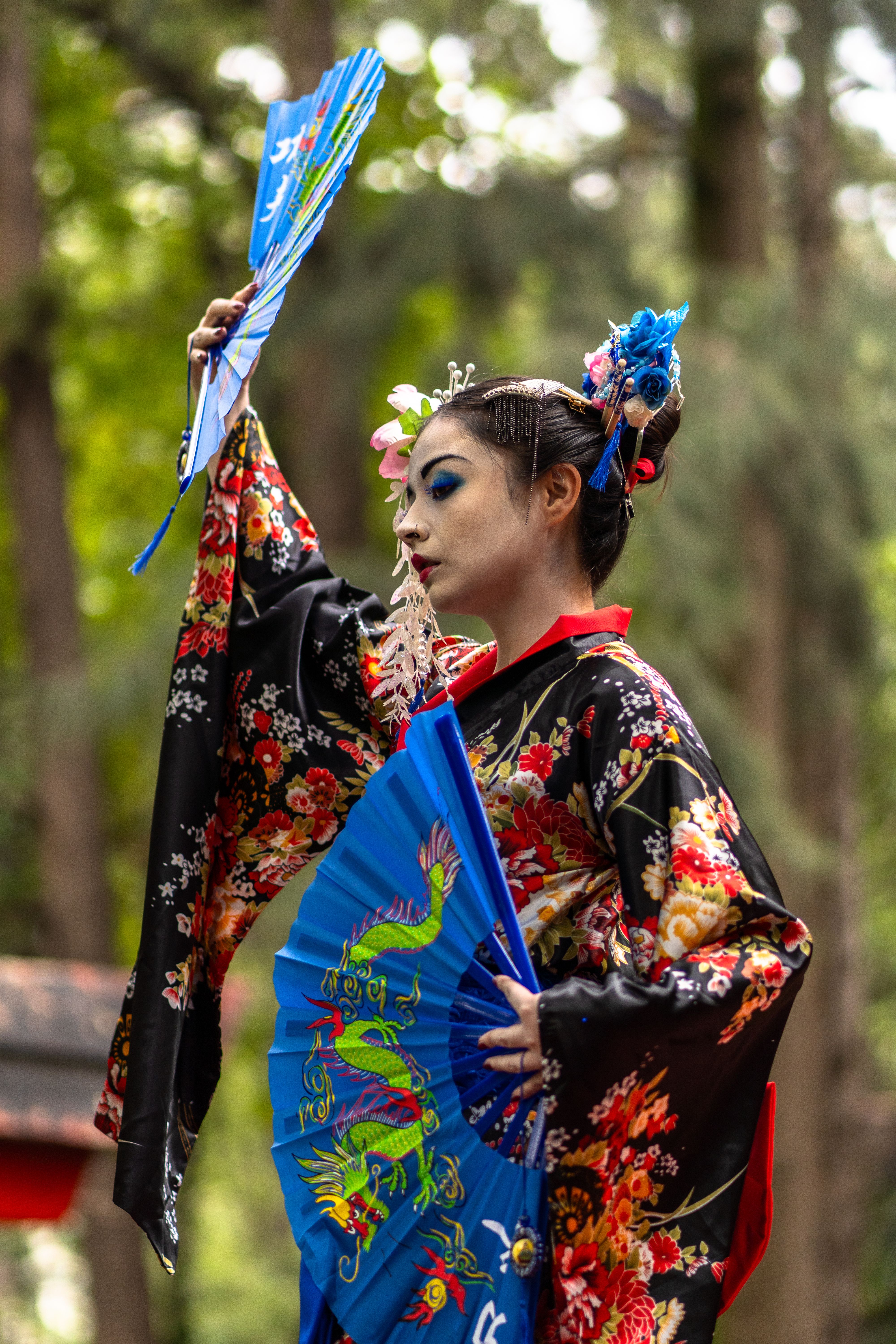 A woman in a traditional geisha costume performs in a public park during a cultural festival.