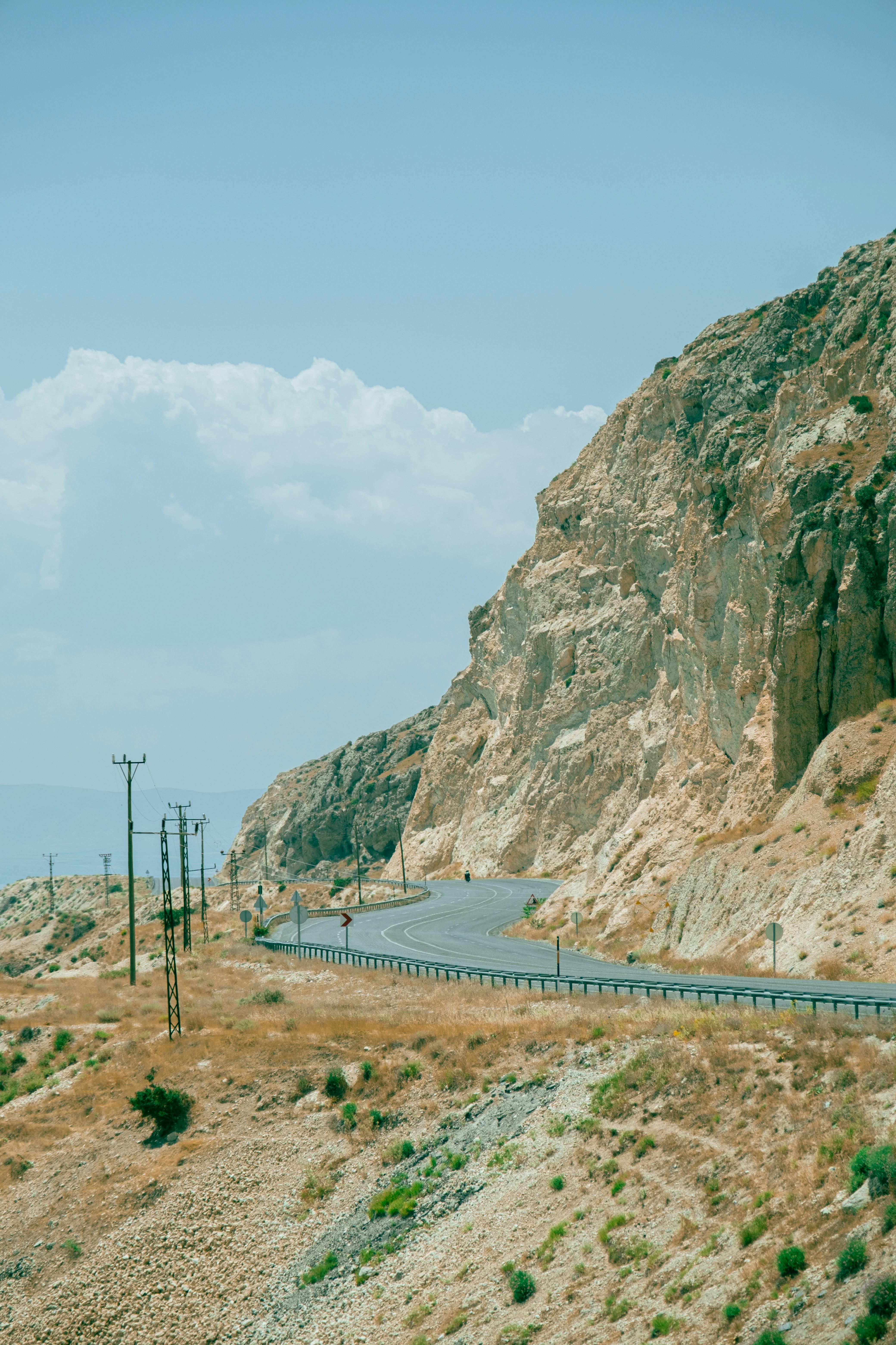 A winding road hugs a steep coastal cliff under a clear blue sky, perfect for travel inspiration.