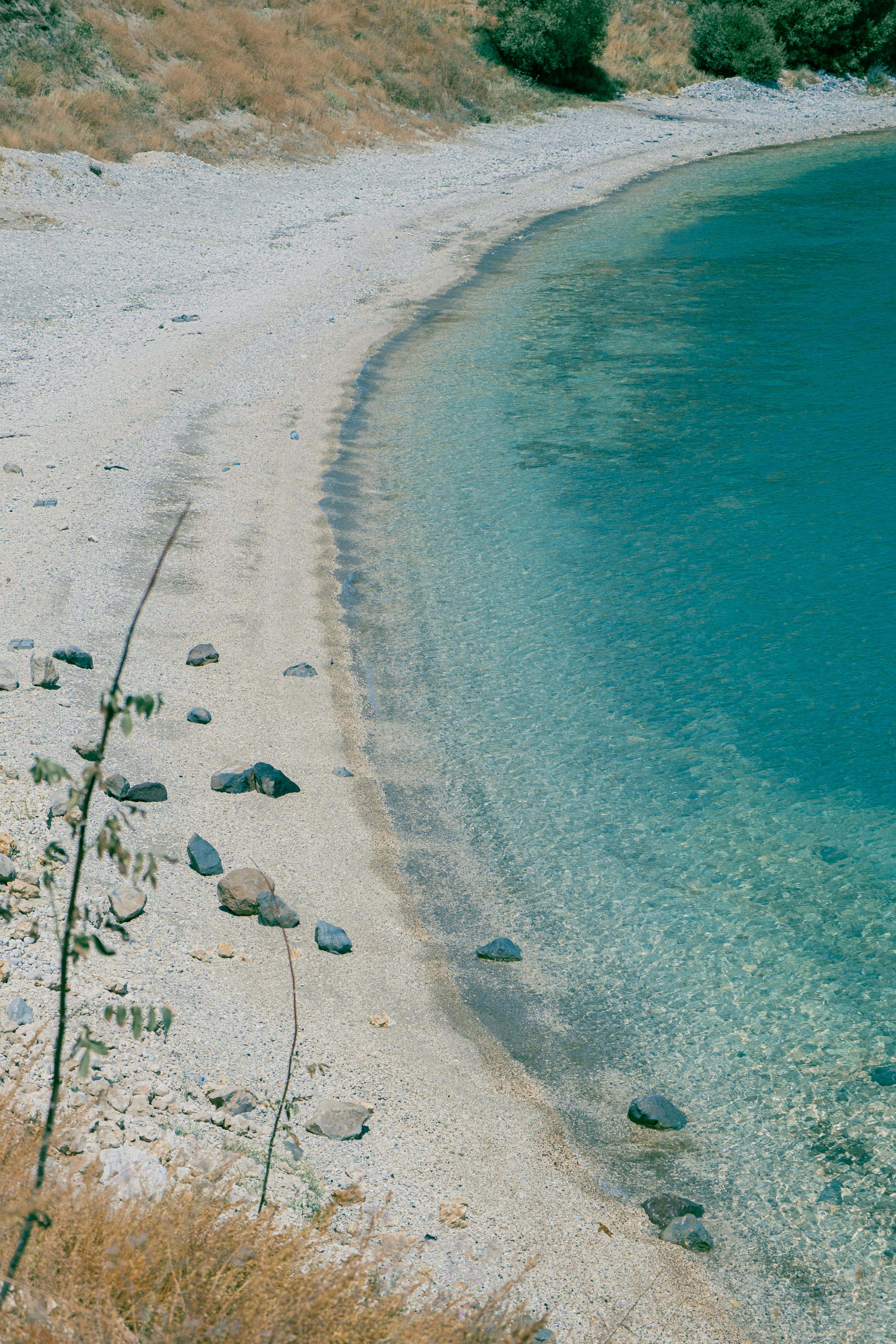A tranquil remote beach with clear turquoise waters and rocky shore under a bright summer sun.