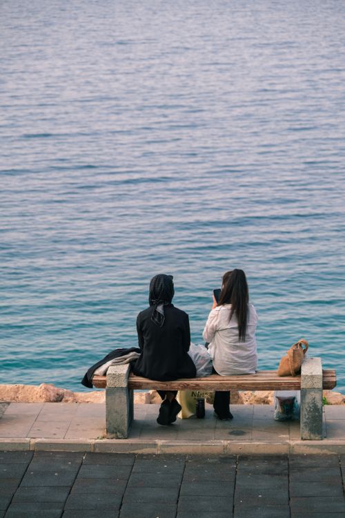 Free Two women enjoying a peaceful moment by the seaside, sitting on a bench. Stock Photo