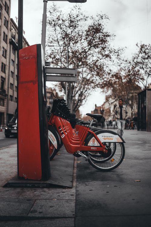 Free Red bike parked at a station in a bustling city street, capturing urban life and transportation. Stock Photo