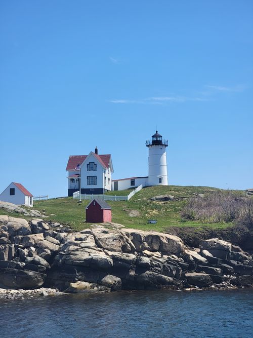 Free A scenic lighthouse and house on a rocky shoreline under a clear blue sky. Stock Photo