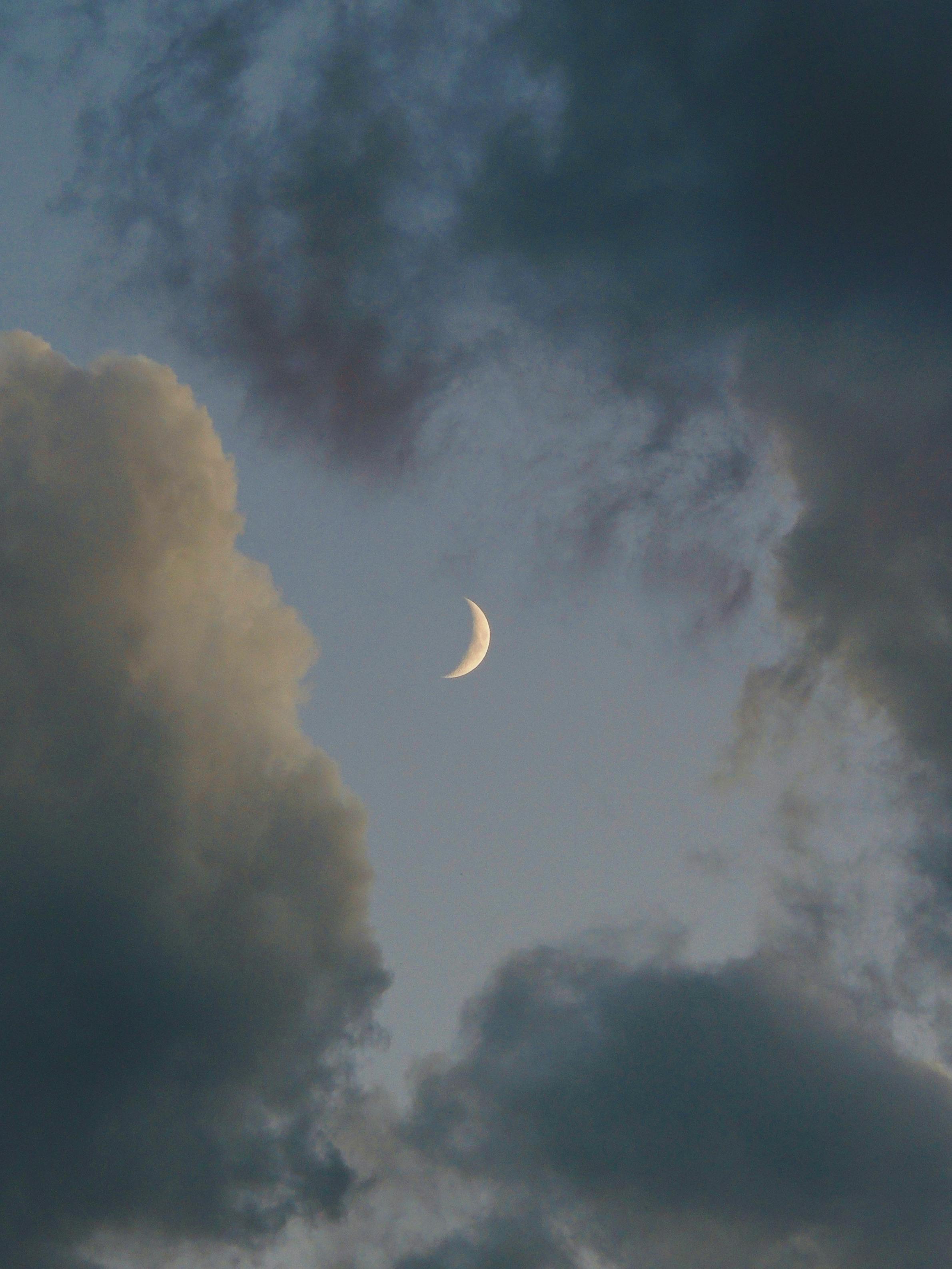 A serene crescent moon framed by dramatic clouds in a twilight sky.
