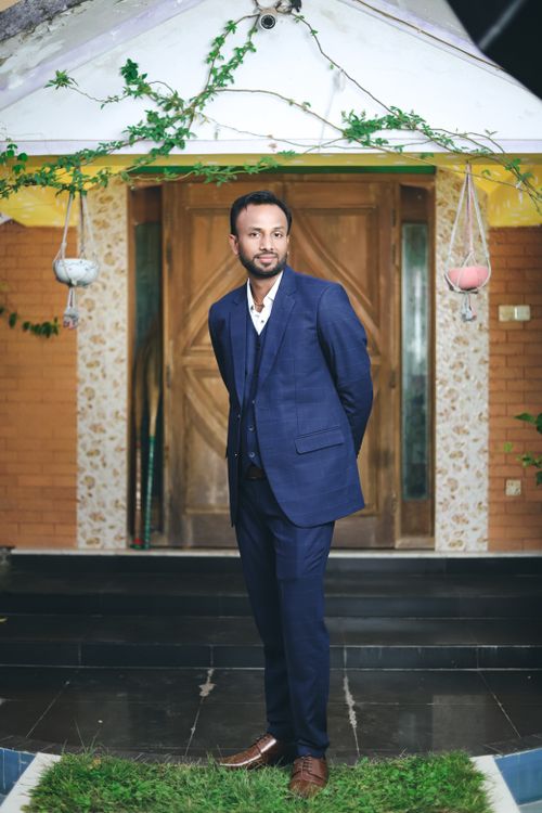 Free A well-dressed man in a blue suit poses outside a wooden door, exuding confidence and style. Stock Photo