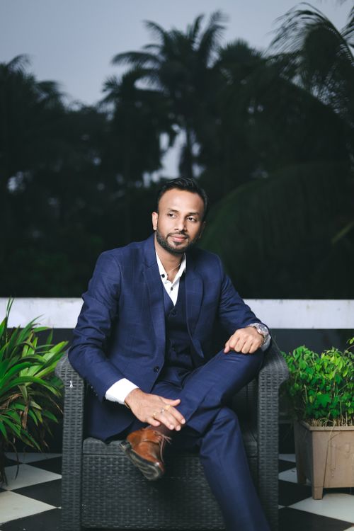 Free A stylish man in a blue suit sits outside amidst lush greenery, exuding elegance. Stock Photo