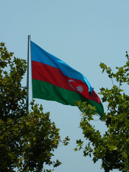 Free Azerbaijan national flag waving in the wind among trees against a clear sky. Stock Photo