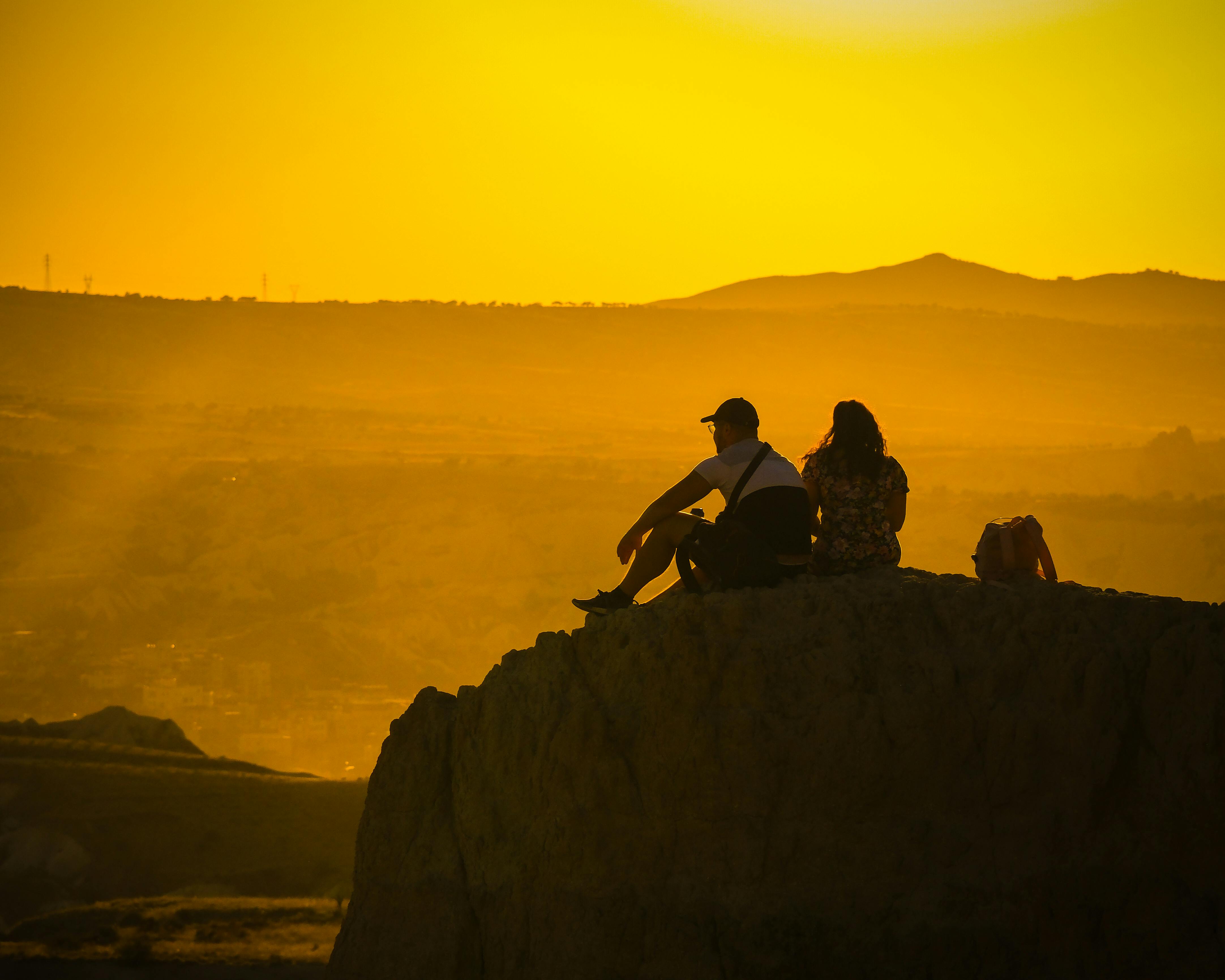 two people sitting on a rock at sunset