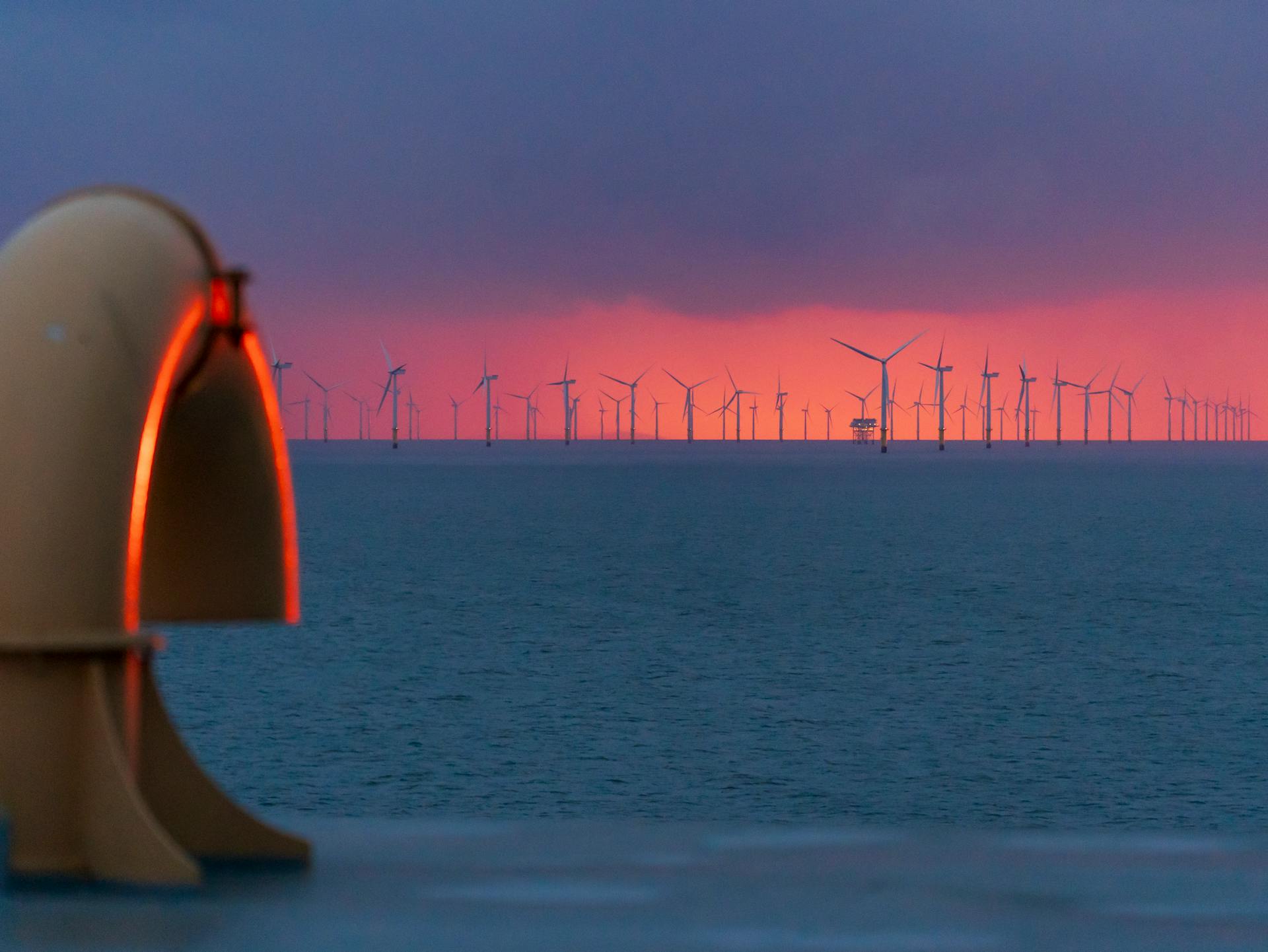 A vibrant sunset over an offshore wind farm captured from the coastline, highlighting renewable energy.