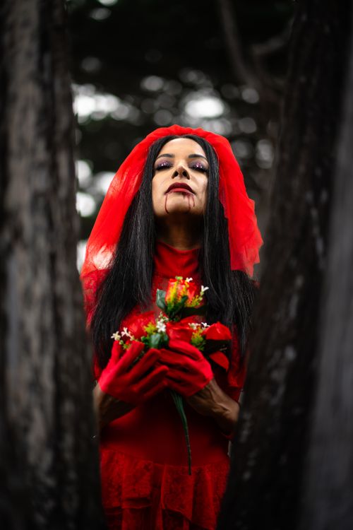 Free Spooky portrait of a woman in a red Halloween costume holding flowers outdoors. Stock Photo