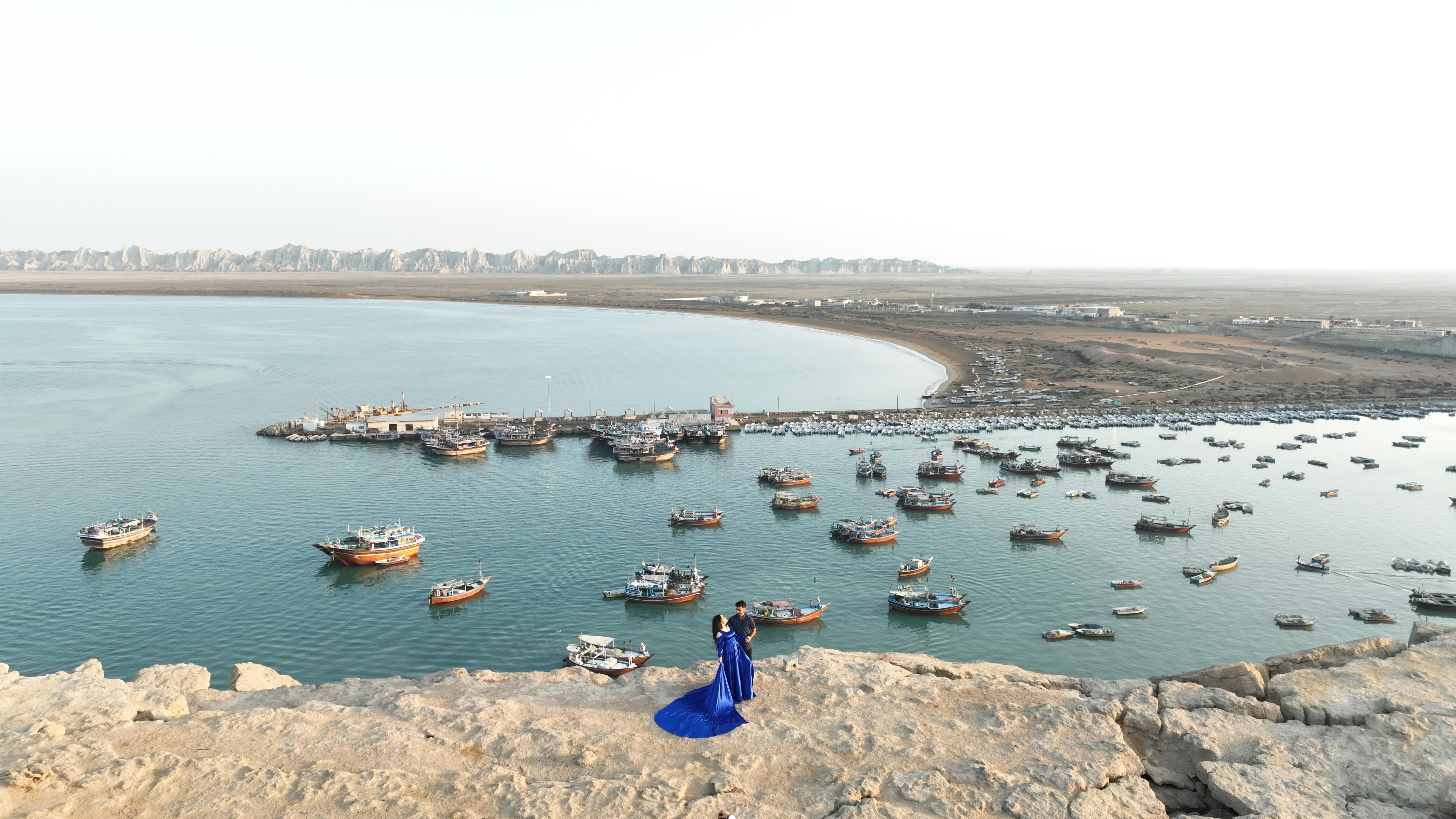 An aerial view of Chabahar harbor with numerous boats and a couple standing on a rock.