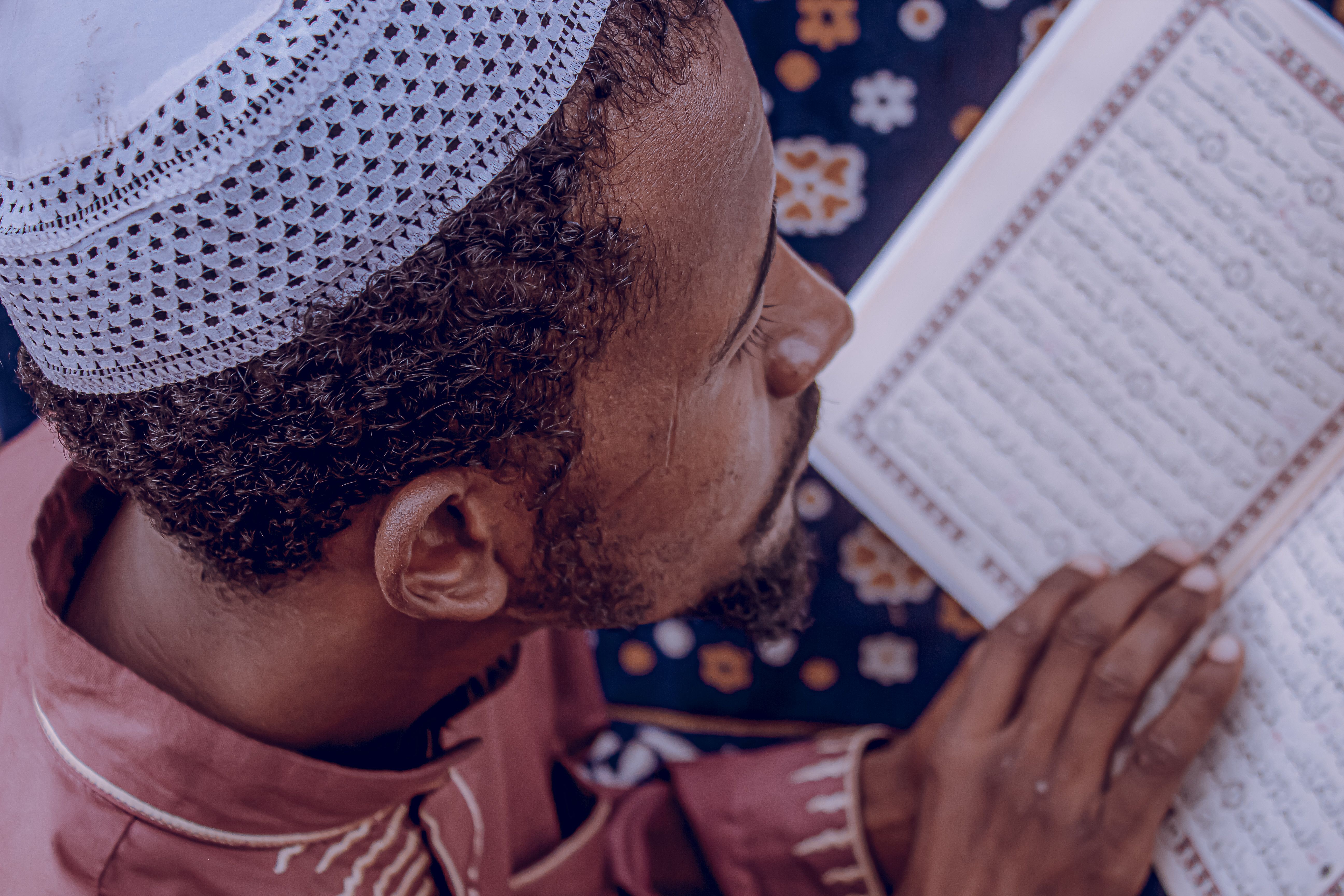 A man in traditional attire reading a religious text indoors, focused on reflection and spirituality.